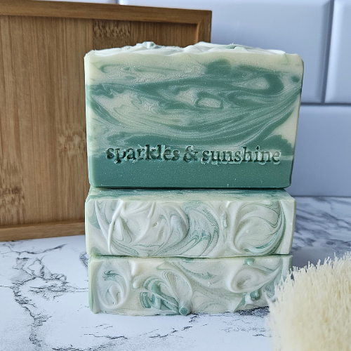 Picture of forest green soap with creamy swirls stacked next to a wood box.