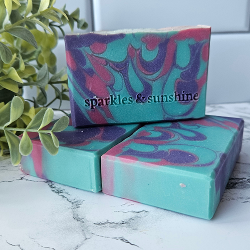 Picture of three bars of turquoise soap with purple and pink swirls.